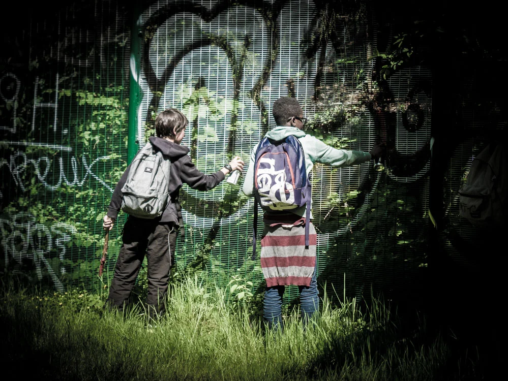 enfant qui font du graffiti sur un grillage à la petite ceinture aux buttes chaumont à paris